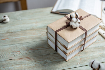 Stack of beautifully wrapped craft paper books, tied with ribbon and decorated with cotton, on a wooden table. Concept of reading and books as a gift. Copy space
