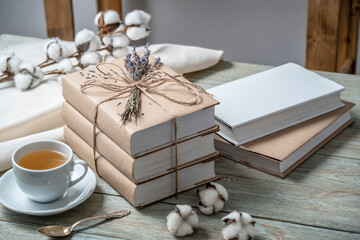Neat, beautiful stack of books with craft paper covers, wrapped in rope and decorated with lavender flowers, and a cup of tea on a wooden table. Concept of a cozy atmosphere for reading