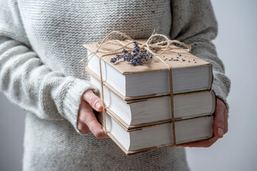 Woman is holding a stack of paperback books wrapped with string and decorated with lavender. Closeup