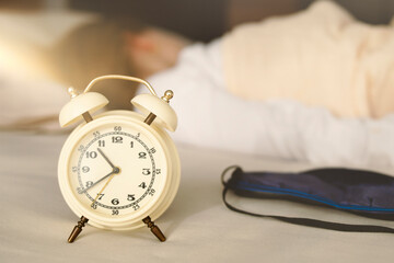 Close-up of an alarm clock and sleep mask, on a blurred background the girl sleeps with her back...
