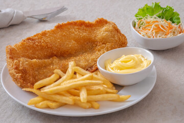 Crispy fish and chips on white plate and vegetable salad in bowl