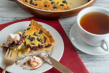 Fresh slice of cherry pie with ice cream and white cup with tea on a wooden background