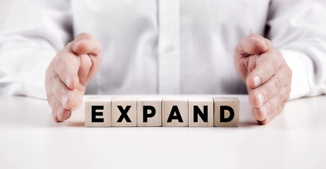 Businessman hands covers the wooden cubes with the word expand.