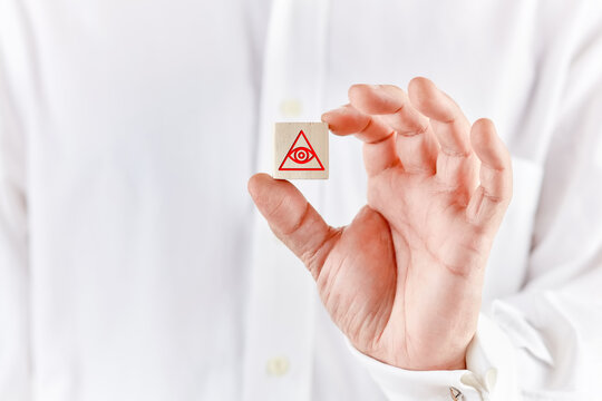 Mason hand holds a wooden cube with the eye of providence or all seeing eye of god symbol.