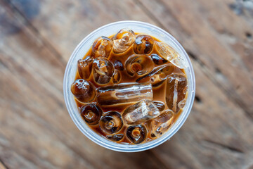 Iced coffee or latte top view on wooden background. Black coffee with ice in plastic glass, close up
