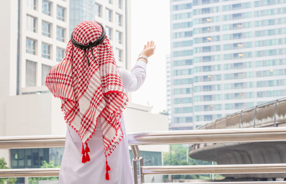 Rear view of young business arab middle eastern muslim man standing while raised hands and praying in city