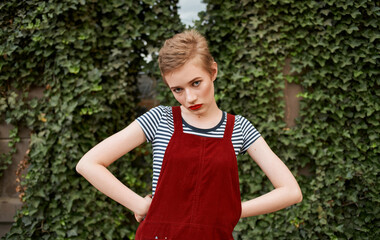 portrait of a blonde with a short haircut bright makeup Red sundress and green leaves of bushes in the background