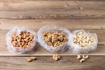 Walnuts, almonds, cashews in plastic bags on a natural wooden background. Copy space.