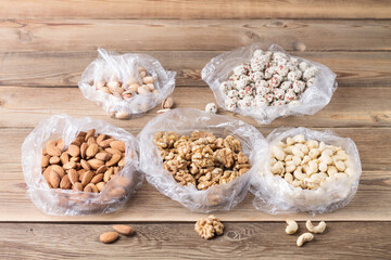 Walnuts, almonds, cashews, hazelnuts and pistachios in plastic bags on a natural wooden background. Superfoods.