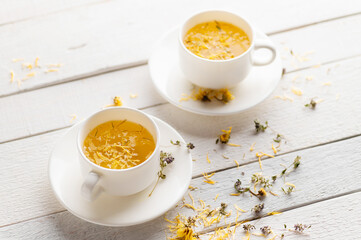 two cups of aromatic flower tea, soothing, alternative medicine, medicinal on white wooden background