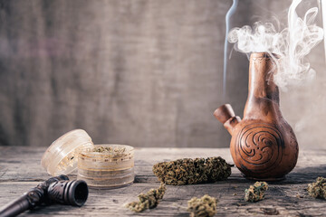 On the wooden surface is an old clay bong with medical marijuana that is smoking