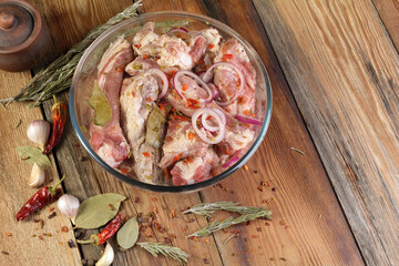 Pork ribs, sliced and marinated with onions. Shish Kebab meat in a glass bowl and spices on a wooden rustic table.Selective focus, close-up, top view.
