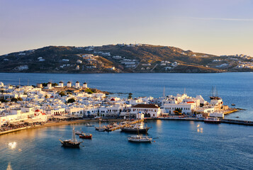 Fototapeta na wymiar Beautiful sunset view over Mykonos, Cyclades, Greece, harbor and port. Golden hour, ships, whitewashed houses. Vacations, Mediterranean lifestyle.