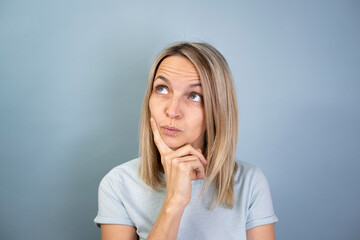 pretty young blond attractive woman posing on blue background and thinking in studio