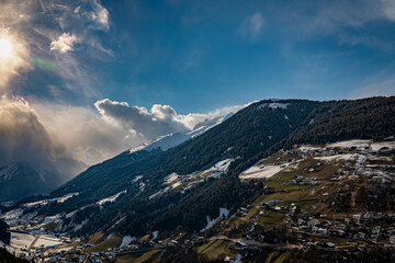 Fototapeta na wymiar Clouds, snow mountains and Tyrolean village in the foreground.2021