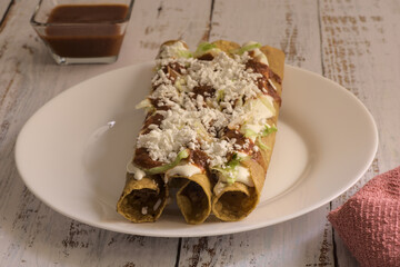 Traditional Mexican food, golden meat tacos (flautas) with red sauce.
