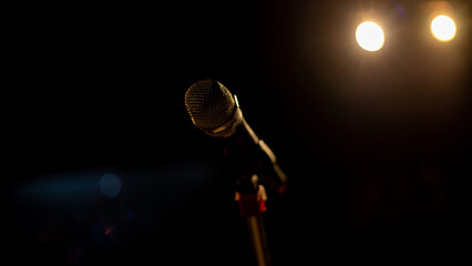 Side view of micrphone on stand sitting on empty stage with lights shinning in background