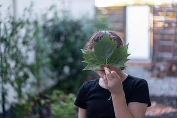 young girl child holding a green leaf in front of her face