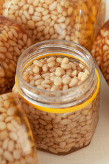 Pine nut with honey in a transparent jar. The jar is open. Nearby pine nuts. Banks in the background. Place for a label. Close-up. Light background.