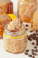 Pine nut with honey in a transparent jar. There is a wooden spoon with honey and nuts on the tank....