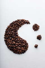 Yin yang symbol with decreasing drops of yin made of dark roasted coffee beans on white paper background with texture and shadows.  Conceptual composition. Relaxation, equilibrium and transcedence