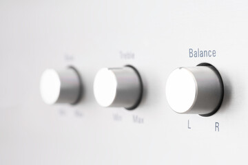 Rotary knobs on an amplifier with gray metal background. Focus on the right button: balance. Being in balance