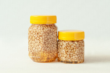 Pine nut with honey in a transparent jar with a yellow lid. A smaller jar with nuts and honey is...