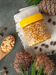 Pine nut with honey in a transparent jar. Yellow cover. Next is a spoon with honey and pine nuts. Cones and needles. View from above. Place for a label.