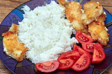 White rice with fried fish and tomatoes in a plate on the table