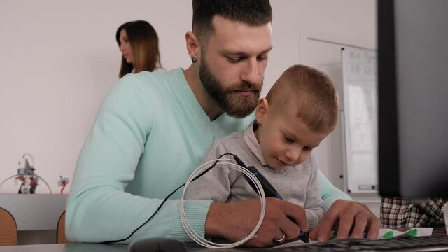 A father and his little son make a 3d plastic model with a 3D pen in a school.