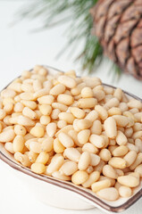 Peeled pine nuts in a cup. In the background there is a cedar cone and needles. Close-up. Macro. White background.