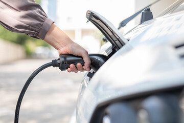 Close up, side view shot, selective focus of a woman's hand grabbing, plugging, holding the EV charger plug handle in front of an electric car. Sustainable energy concept