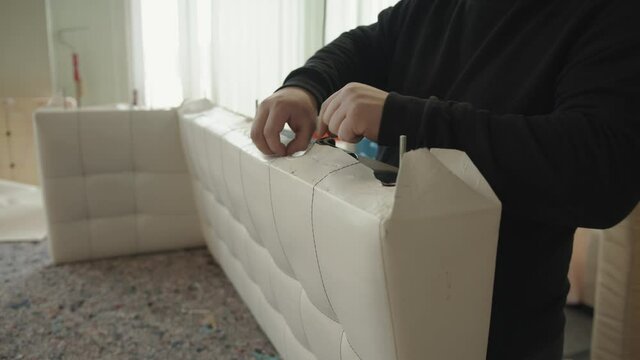A professional craftsman removes staples from sofa parts in a furniture repair and upholstery workshop