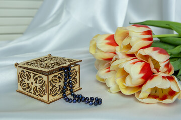 A jewelry box and a bouquet of tulips. Wooden carved jewelry box and pearl necklace. Yellow and red...