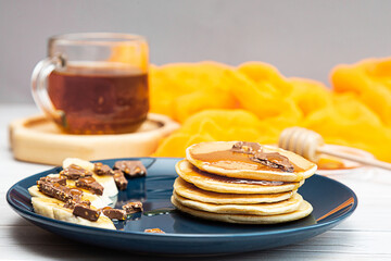 Homemade pancakes with honey, banana and chocolate. Healthy breakfast concept, copy space. A bright still life with a cup of tea, a plate of pancakes