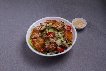 Bowl of traditional caesar salad with chicken and bacon isolated on gray background
