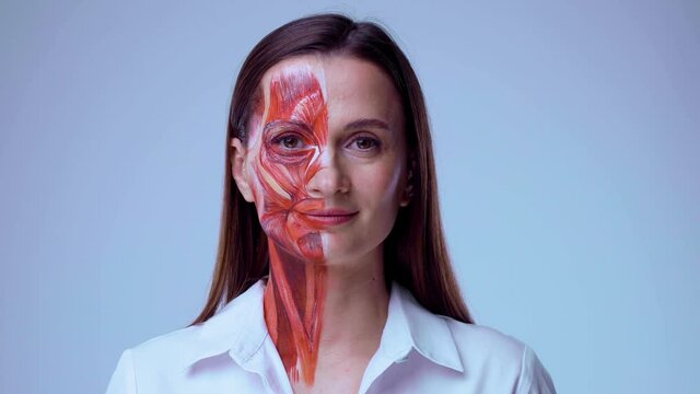 Young woman with half of face with muscles structure under skin. Model for medical training on a light background. Close up video of face human anantomy.