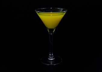 A tequila glass with a yellow cocktail on a black background.