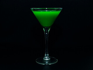 A tequila glass with a green cocktail on a black background.