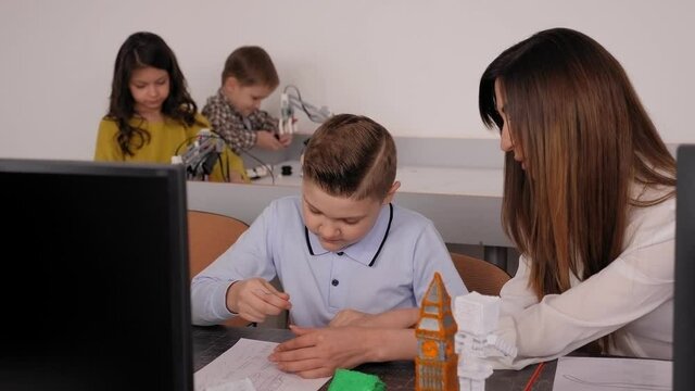 A mother helps her son create a model boat with a 3 d pen at a school.