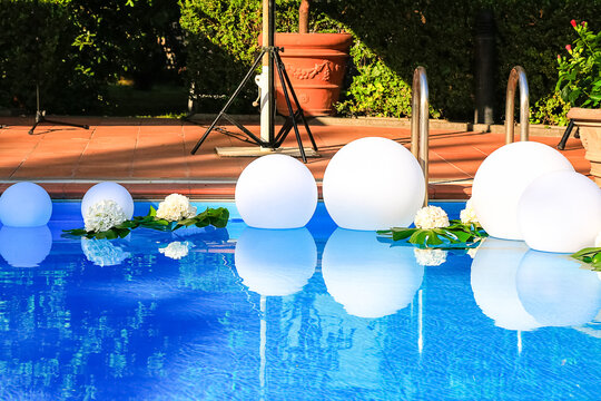 Open air swimming pool decorated with white floating balls and fresh flowers for wedding party. Summer event preparation. Party design. Clean transparent blue water. Background and postcard picture 