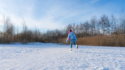 Young woman with a pink scarf having fun while ice skating on a frozen lake in winter