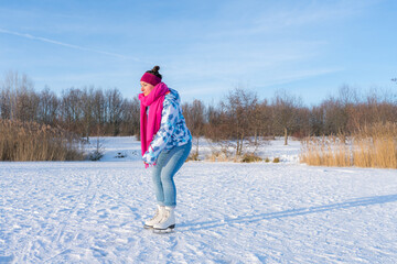 Young woman with a pink scarf having fun while ice skating on a frozen lake in winter