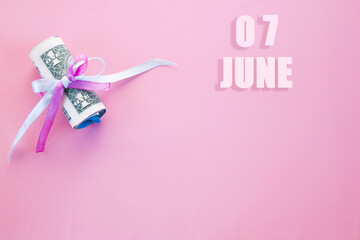 calendar date on pink background with rolled up dollar bills pinned by pink and blue ribbon with copy space. June 7 is the seventh day of the month