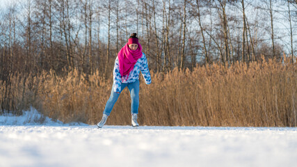 Young woman with a pink scarf having fun while ice skating on a frozen lake in winter