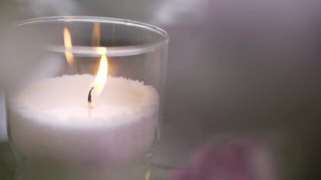 elegant decorative burning candle made of light pink wax in clear glass holder and space for design on blurred background extreme close view