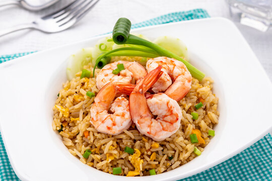Thai shrimp fried rice or khao pad goong, the popular comfort food for many Thais, served on the deep white plate together with vegetables like cucumber slices and scallion.