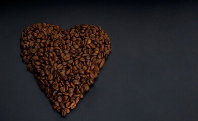 Roasted arabica coffee beans laid out in the shape of a heart, lie on a dark wooden background close up