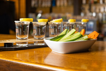tequila shot on bar table with lemon, salt, cucumber and carrot