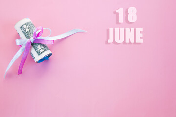calendar date on pink background with rolled up dollar bills pinned by pink and blue ribbon with copy space. June 18 is the eighteenth day of the month